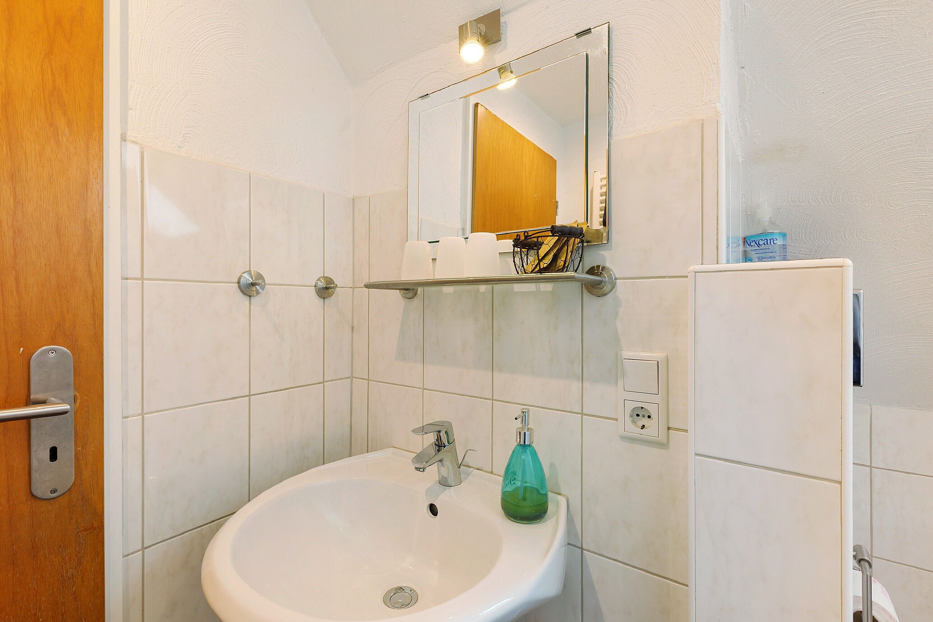 Een badkamer met een witte wastafel, een spiegel en een plank met toiletartikelen.