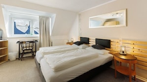 Ett hotellrum med två sängar, ett skrivbord, en stol, en spegel och ett fönster med gardiner.