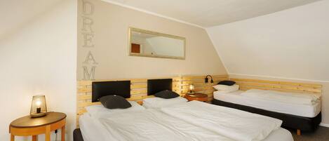 A hotel room with two beds, a bedside table with a lamp, a mirror on the wall, and a ceiling light fixture.