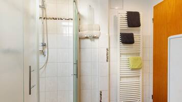 Een badkamer met een douchecabine van glas, een witte handdoekhouder met meerdere handdoeken, en een houten deur.
