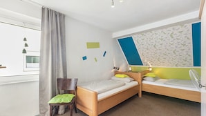 Un dormitorio con dos camas de madera, una silla, un escritorio y un ventanal con cortinas.