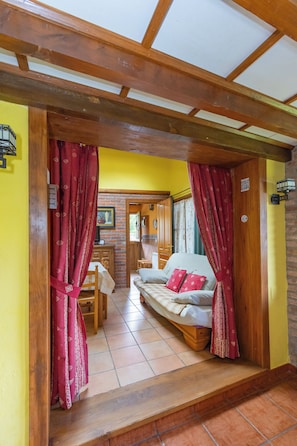 Une pièce avec un plafond en bois, un canapé avec des coussins rouges, une table à manger et un coin cuisine visible à travers une porte ouverte.