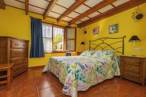 Une chambre à coucher avec un lit, une commode en bois, une table de chevet et une fenêtre avec des rideaux.