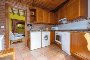 Une cuisine compacte avec des meubles en bois, un lave-linge, un four à micro-ondes et un coin repas avec une chaise.