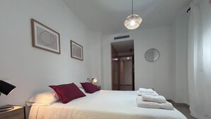 A neatly made bed with white bedding and two red pillows, a bedside lamp, and a hanging light fixture. - Nomads' Triangle" Central Park - Ruzafa - Turia (València)