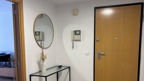 A room with a wooden door, a small console table with a vase, a wall-mounted telephone, and a ceiling light. - Nomads' Triangle" Central Park - Ruzafa - Turia (València)