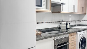 A modern kitchen with white cabinets, a built-in oven, a microwave, a toaster, and a washing machine. - Nomads' Triangle" Central Park - Ruzafa - Turia (València)