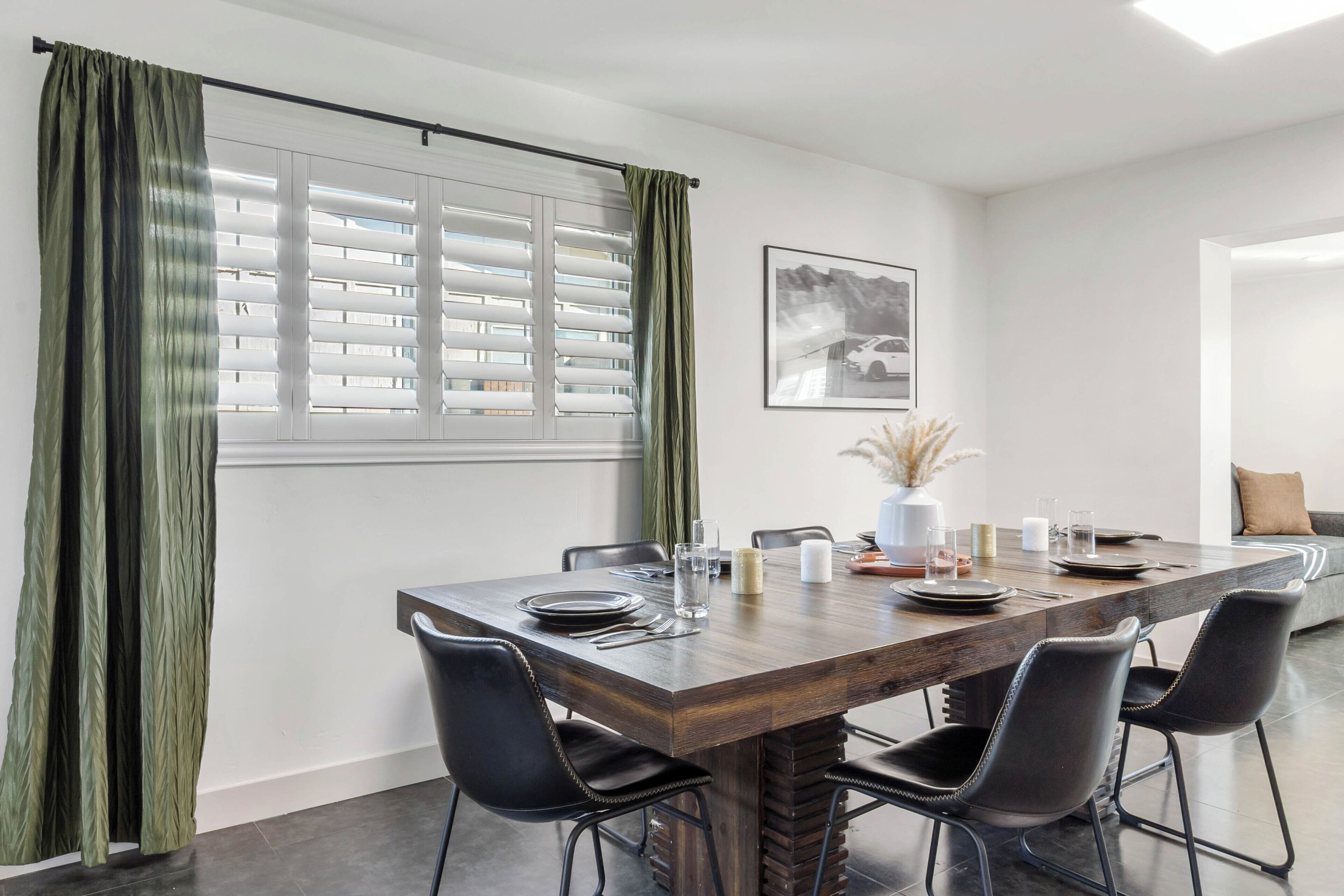 A dining area with a wooden table, black chairs, and a window with blinds.