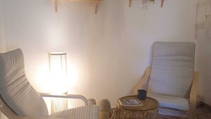 A room with two armchairs, a small round table with a book and a cup, and a lamp. There are two shelves with decorative items and plants. - Country house in the Sierra Nevada- Almería. Nature, hiking and relaxation (Abrucena)