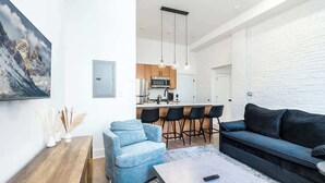 A modern living room with a sofa, armchair, and coffee table. A kitchen with bar stools is visible in the background. - Old City - Luxury Waterview The Heritage (Philadelphia)