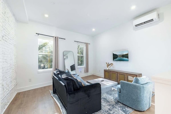 Una sala de estar moderna con un sofá negro, un sillón gris, un mueble de madera y un televisor montado en la pared.