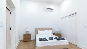 Et soveværelse med seng, sengeborde, aircondition og et garderobeskab.