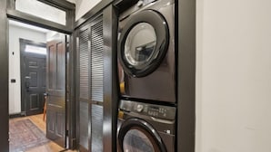 A laundry room with two stacked front-loading washing machines, a closed door, and a wooden floor. - Spacious, Historic 4Br Logan Circle Townhome (Washington D.C.)