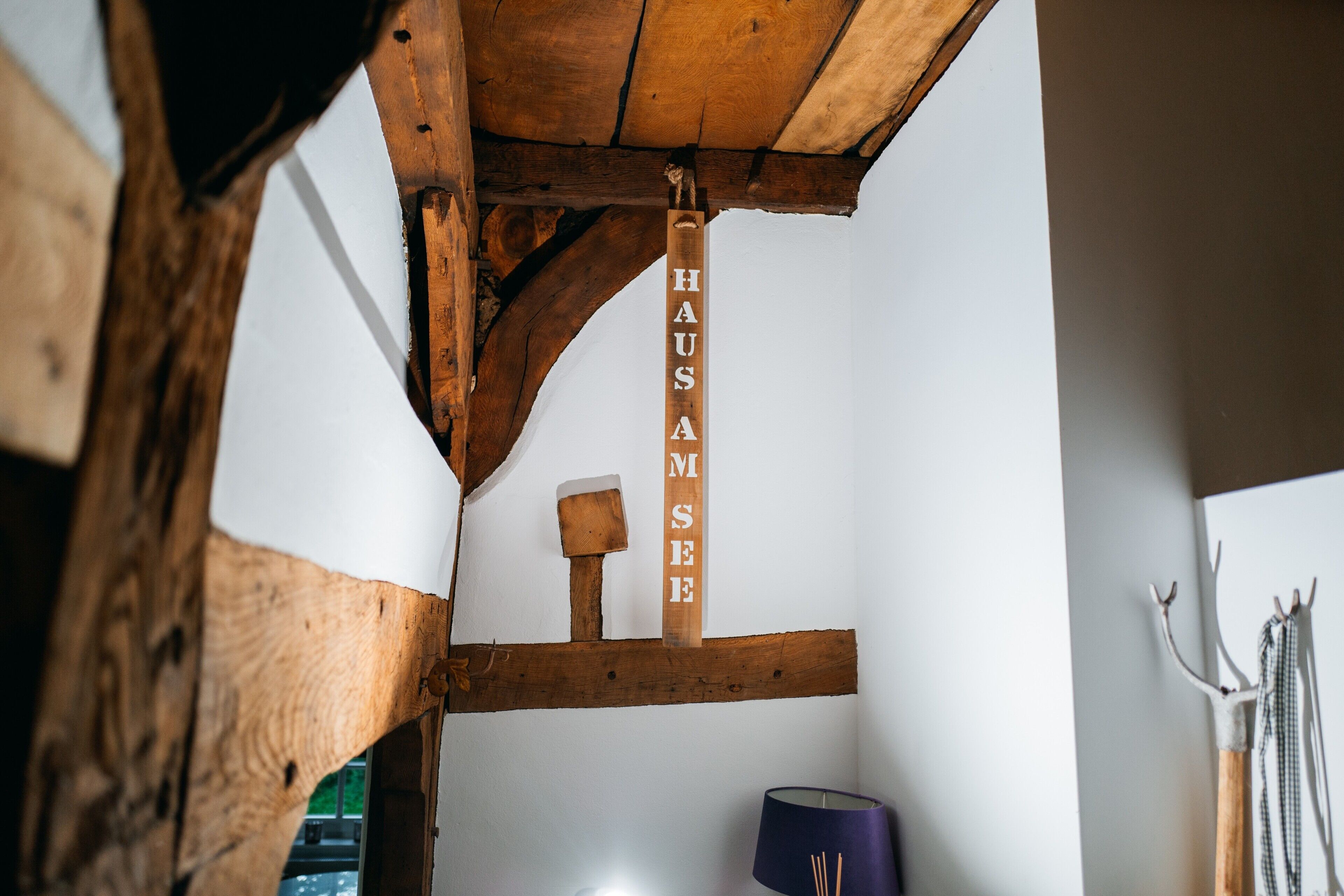 Un interior rústico de madera con vigas a la vista, un letrero de madera que dice 'HAUS AM SEE' y una lámpara.