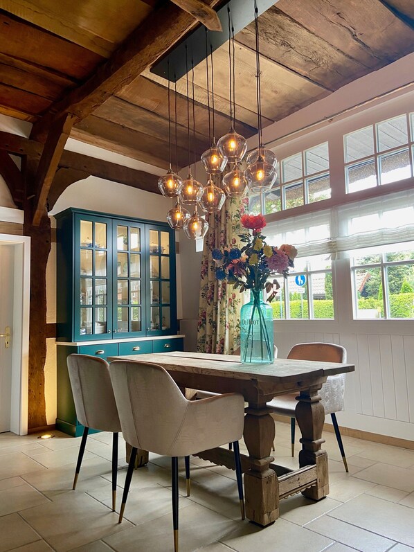 Un comedor con una mesa de madera, sillas, un florero con flores y un armario azul.