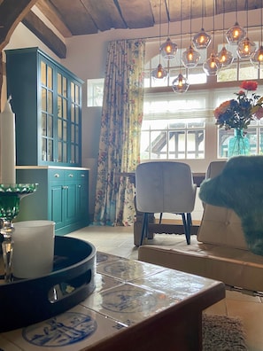 Una habitación con un armario azul, una mesa con mantel de estampado azul y blanco, una silla con cojín azul y un florero con flores en el alféizar de la ventana.