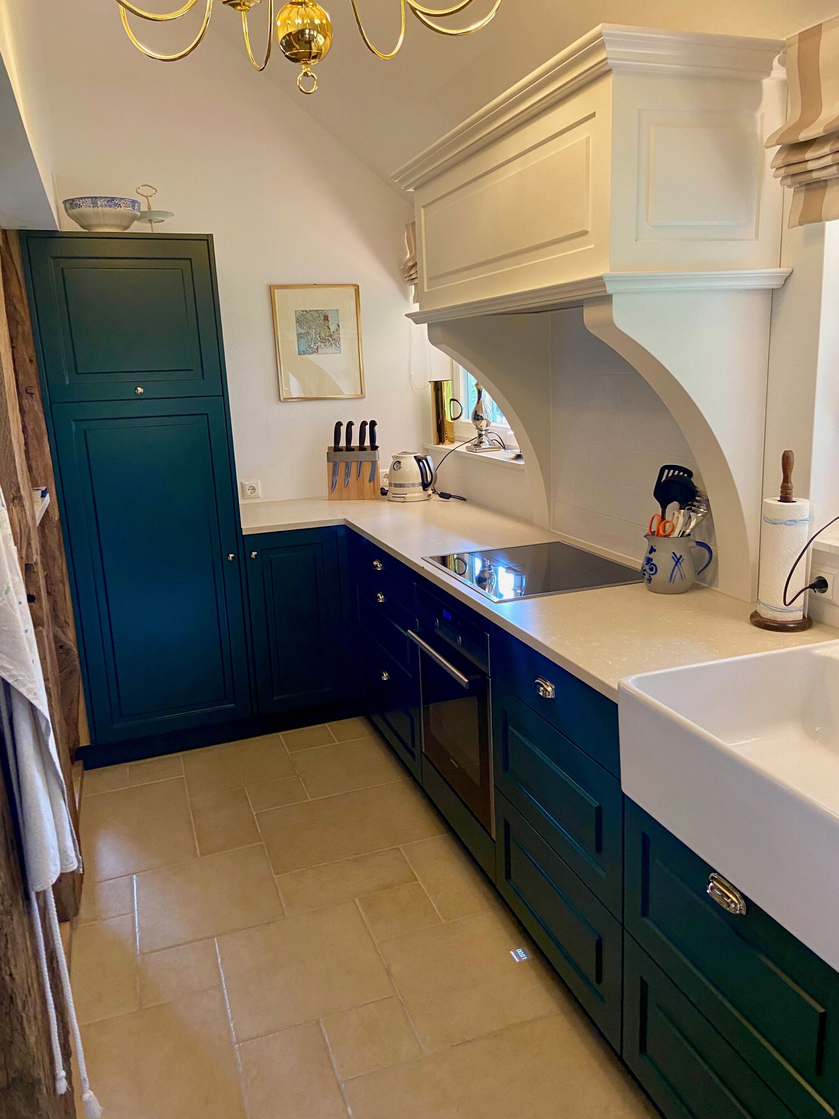 Een keuken met blauwgroene kastjes, een wit aanrecht, een spoelbak en een raam met uitzicht.