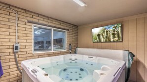 A hot tub in a room with a brick wall, a window, and a cactus painting. - Private Hot Tub & Huge Yard: Phoenix Family Home (Phoenix)
