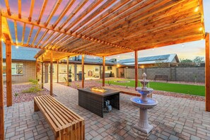 Eine Terrasse im Freien mit einer Holz-Pergola, einer Feuerstelle, einer Bank und einem Brunnen.