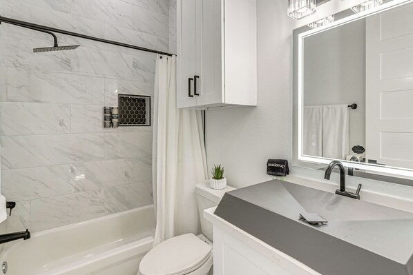 Un baño moderno con bañera, inodoro y un espejo grande sobre el lavabo.
