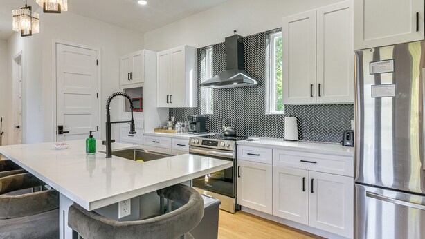 A modern kitchen with white cabinets, stainless steel appliances, and a large island with bar stools. - Sleek, Mod, Luxe: Soccer Fan Home Base in Houston (Houston)