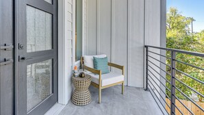 A balcony with a wooden chair and a woven stool, a door with frosted glass panels, and a view of greenery. - Sleek, Mod, Luxe: Soccer Fan Home Base in Houston (Houston)