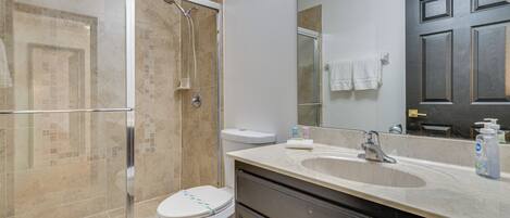 A bathroom with a glass-enclosed shower, a white toilet, a sink with a mirror, and a dark door.