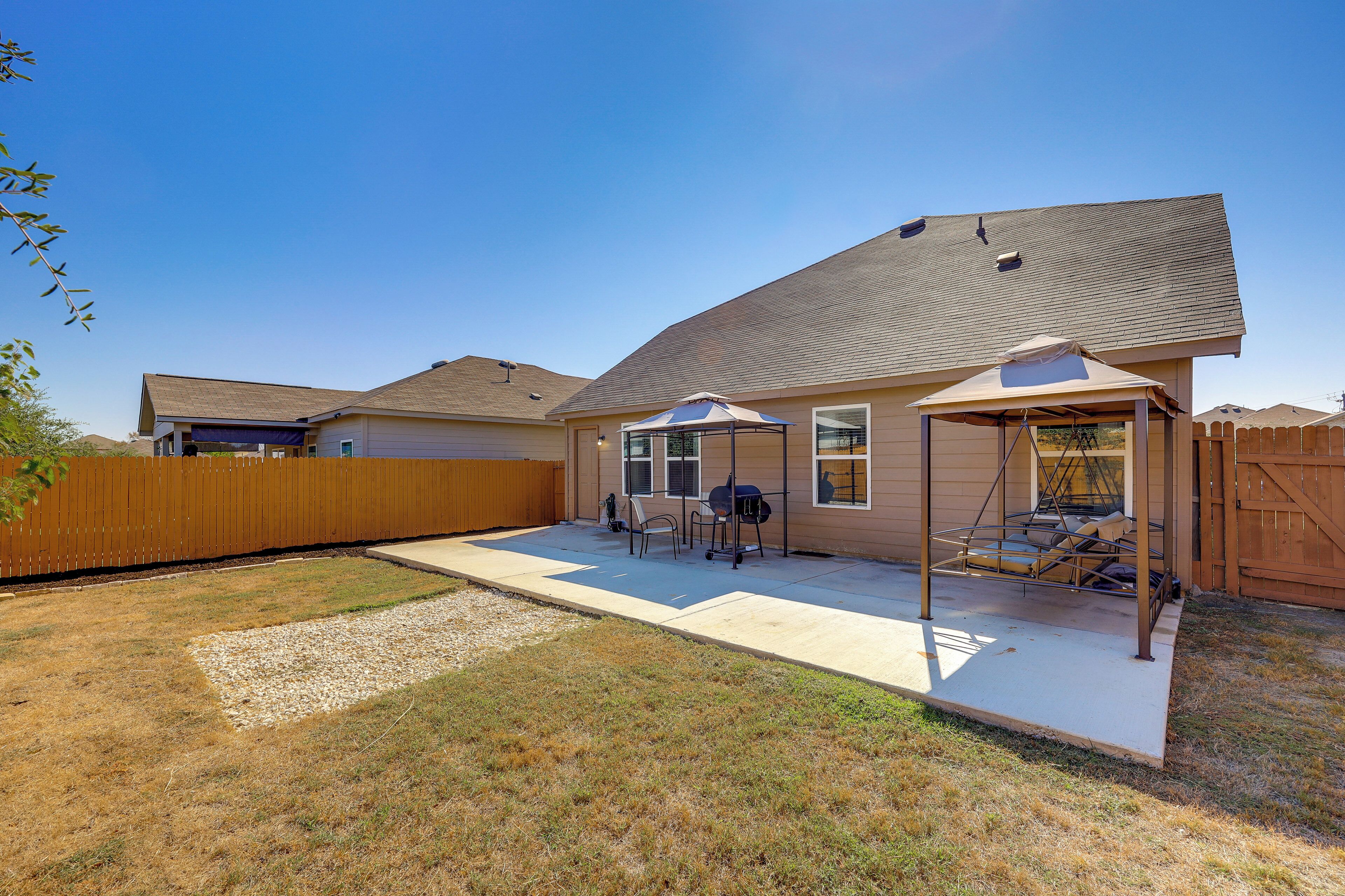 A residential backyard with a covered patio area, a wooden fence, and a clear sky.