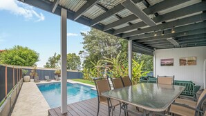 A covered outdoor patio with a pool, a table with chairs, and a view of the backyard. - Lighthouse Beach Coastal Escape (Port Macquarie)
