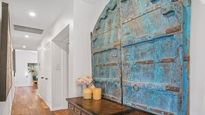 A hallway with wooden flooring, a large blue door, and a wooden dresser with candles. - Lighthouse Beach Coastal Escape (Port Macquarie)
