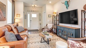 A spacious living room with a leather sofa, a coffee table, a television, and a bookshelf. - Walk to Light Rail! Townhome 9 Mi to Dtwn Denver (Lakewood)
