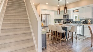 A modern kitchen with a central island, bar stools, and a stainless steel refrigerator. - Walk to Light Rail! Townhome 9 Mi to Dtwn Denver (Lakewood)
