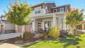 A two-story house with a front porch, a garage, and a landscaped yard with trees and shrubs. - Walk to Light Rail! Townhome 9 Mi to Dtwn Denver (Lakewood)