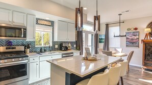 A modern kitchen with white cabinets, a stainless steel stove, and a large island with bar stools. - Walk to Light Rail! Townhome 9 Mi to Dtwn Denver (Lakewood)