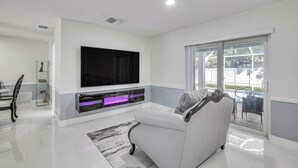 Een moderne woonkamer met een flatscreen televisie, een witte bank en een glazen deur naar een buitenruimte.