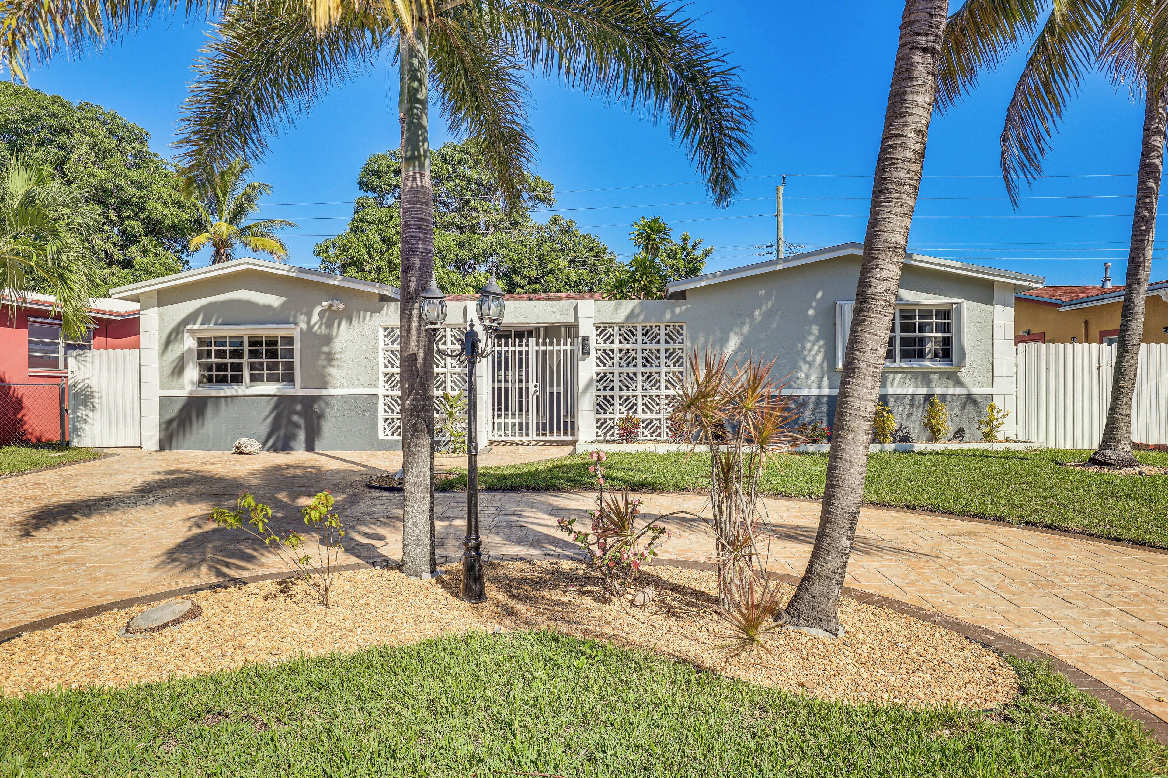 A residential house with a garage, a small garden with palm trees, and a paved driveway.