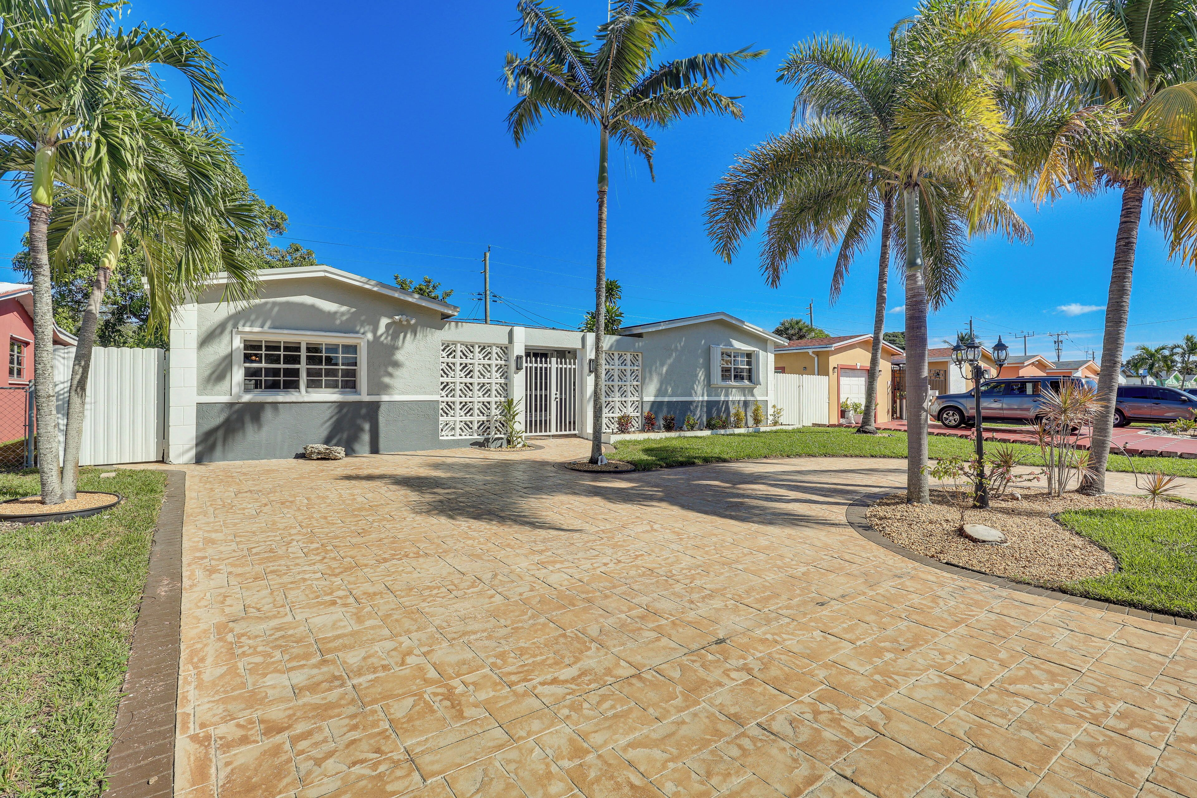 A residential property with a paved driveway, palm trees, and a gated entrance.