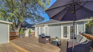 Eine Holzterrasse mit Gartenmöbeln, darunter ein Korbsessel und Stühle, und ein großer Sonnenschirm, der Schatten spendet.