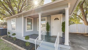 Ein eingeschossiges Haus mit Veranda, einer Tür und einem kleinen Vorgarten mit Backsteinrand und einigen Sträuchern.