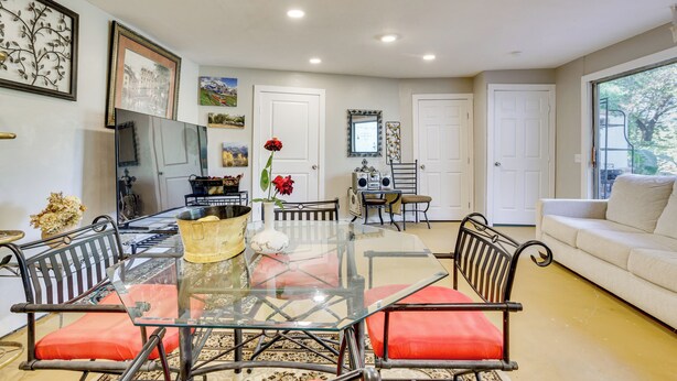 Un comedor con una mesa de vidrio y sillas de metal, un sofá y un televisor en la pared.