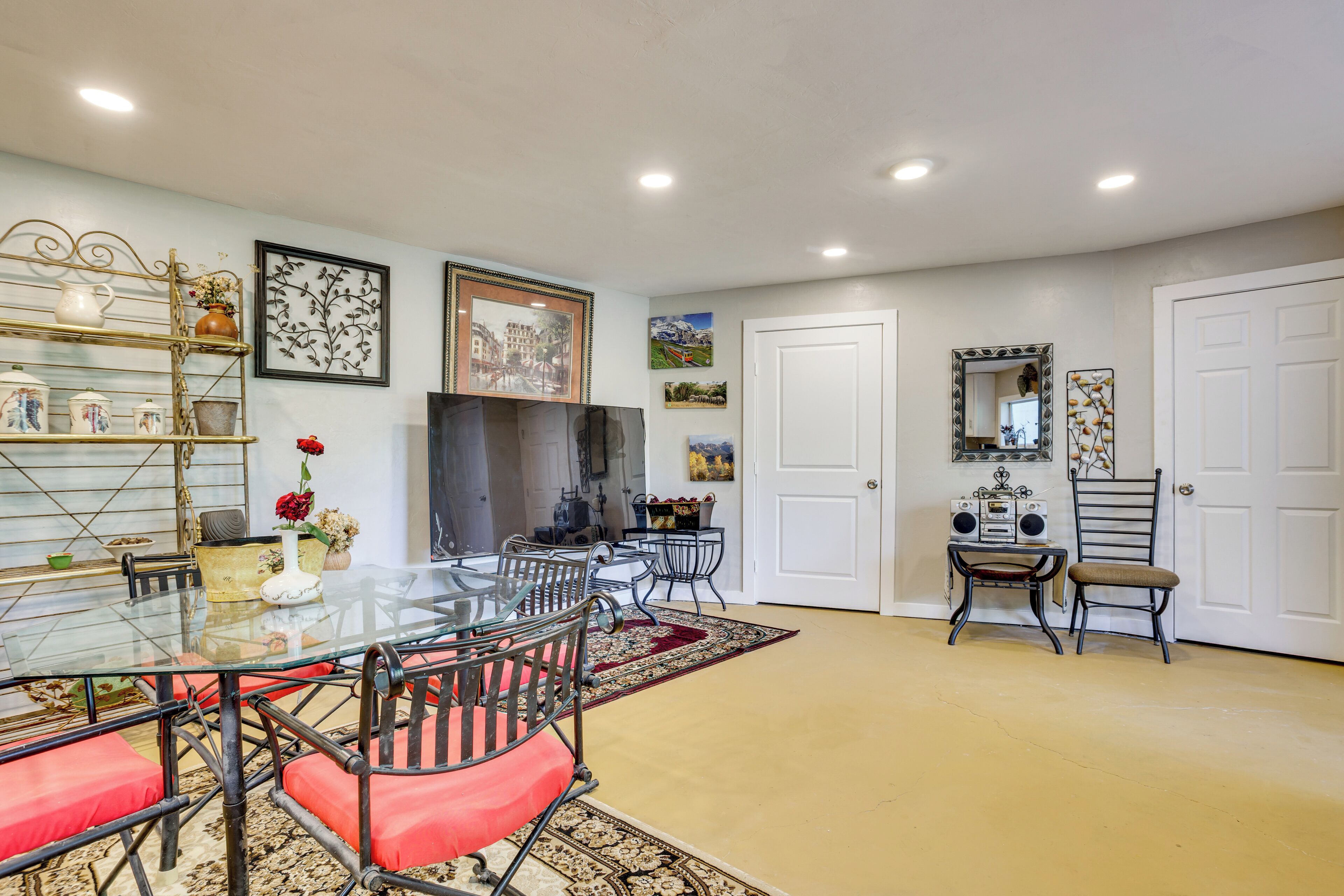 A dining area with a glass table, red cushioned chairs, and a metal shelf with decorative items.