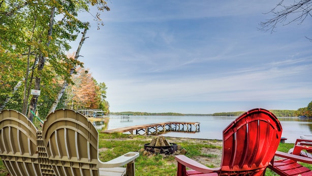 A lakeside setting with Adirondack chairs, a fire pit, and a wooden dock extending into the water. - Land O' Lakes Cabin on Big Portage w/ Fire Pit (Land O' Lakes)