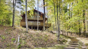 A wooden cabin with a balcony, surrounded by trees and a stone staircase leading up to it. - Land O' Lakes Cabin on Big Portage w/ Fire Pit (Land O' Lakes)