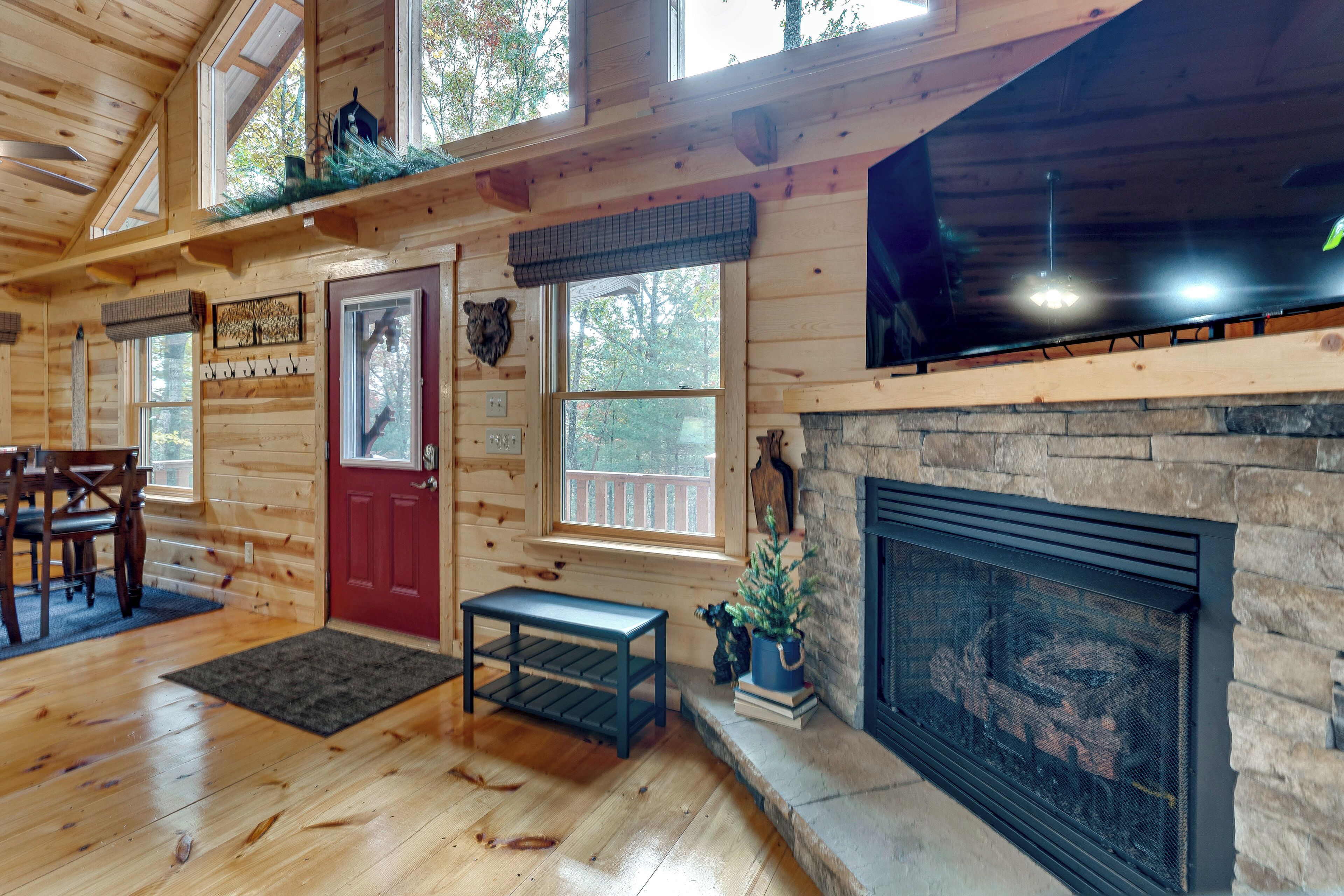 A wooden cabin interior with a fireplace, wooden floors, a red door, and a bench.