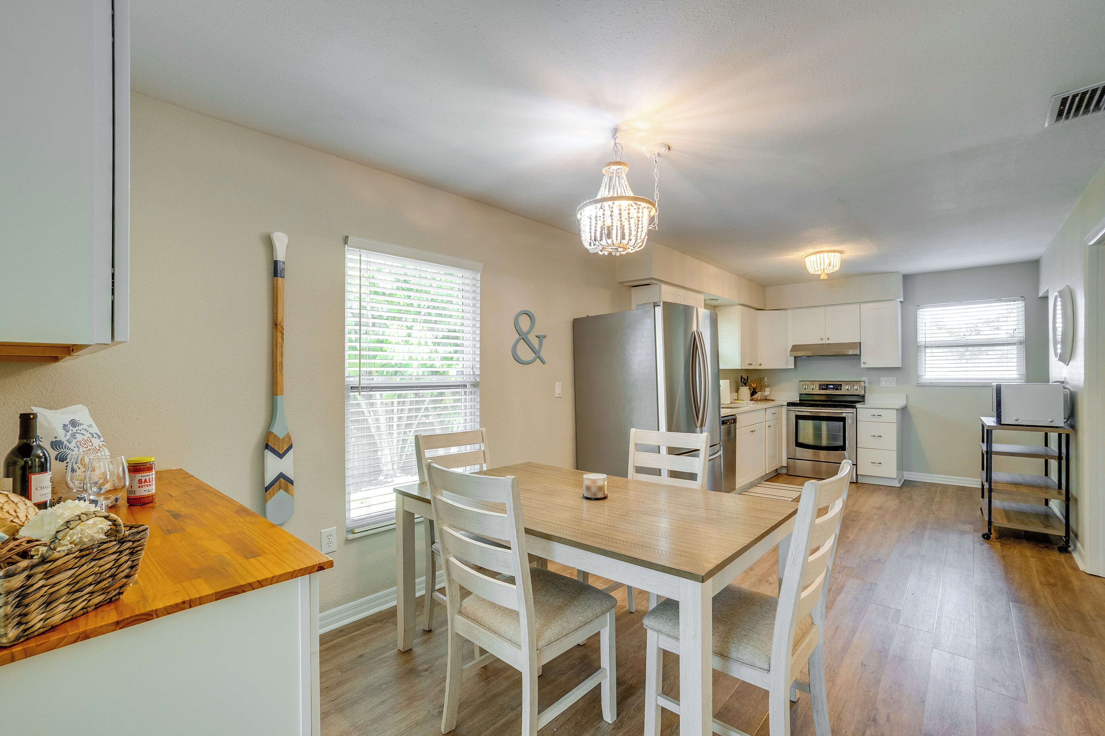 A kitchen with a wooden table, white chairs, a chandelier, and a refrigerator.