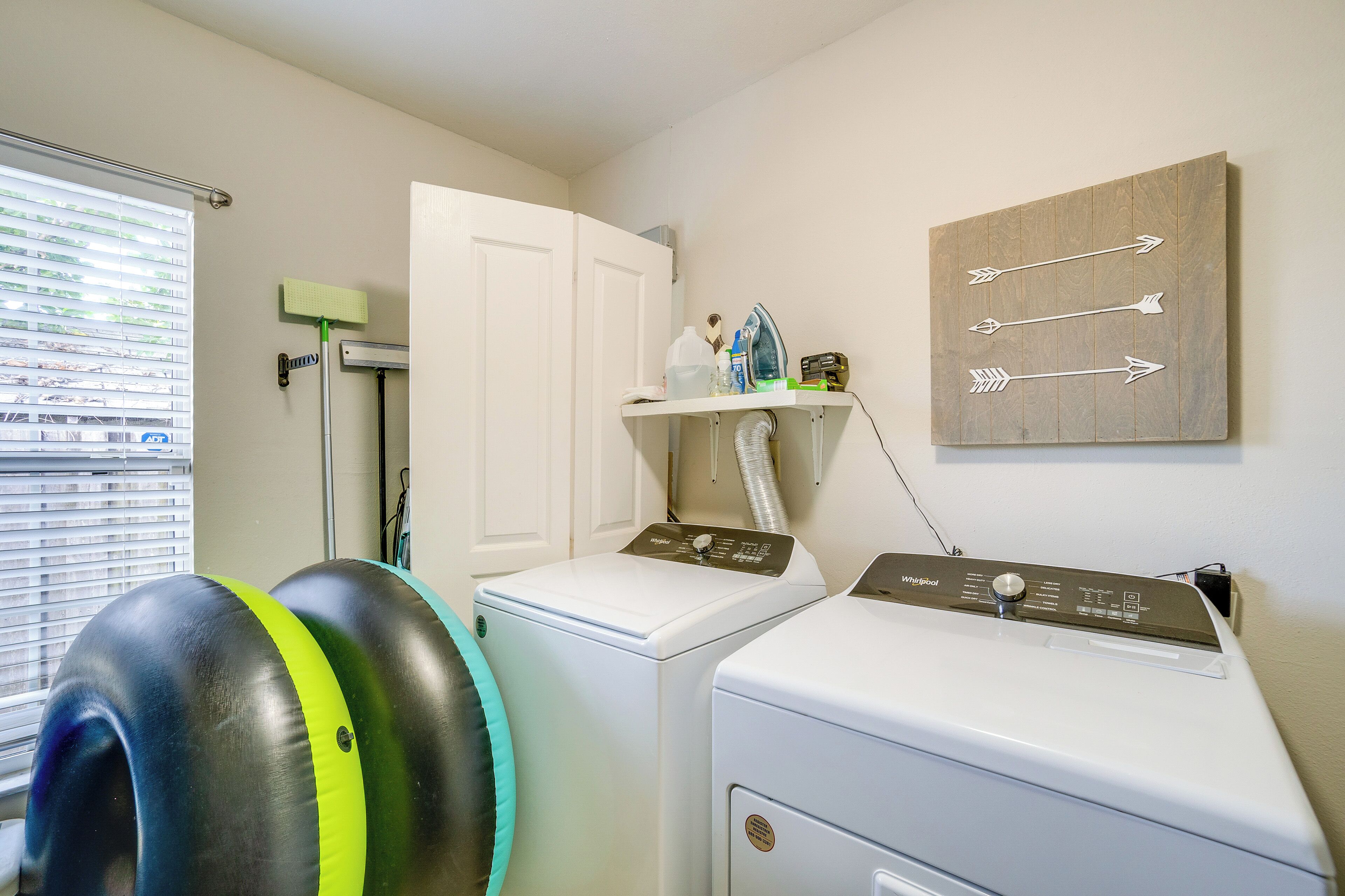 A laundry room with two front-loading washers and dryers, a drying rack, and a shelf with laundry supplies.