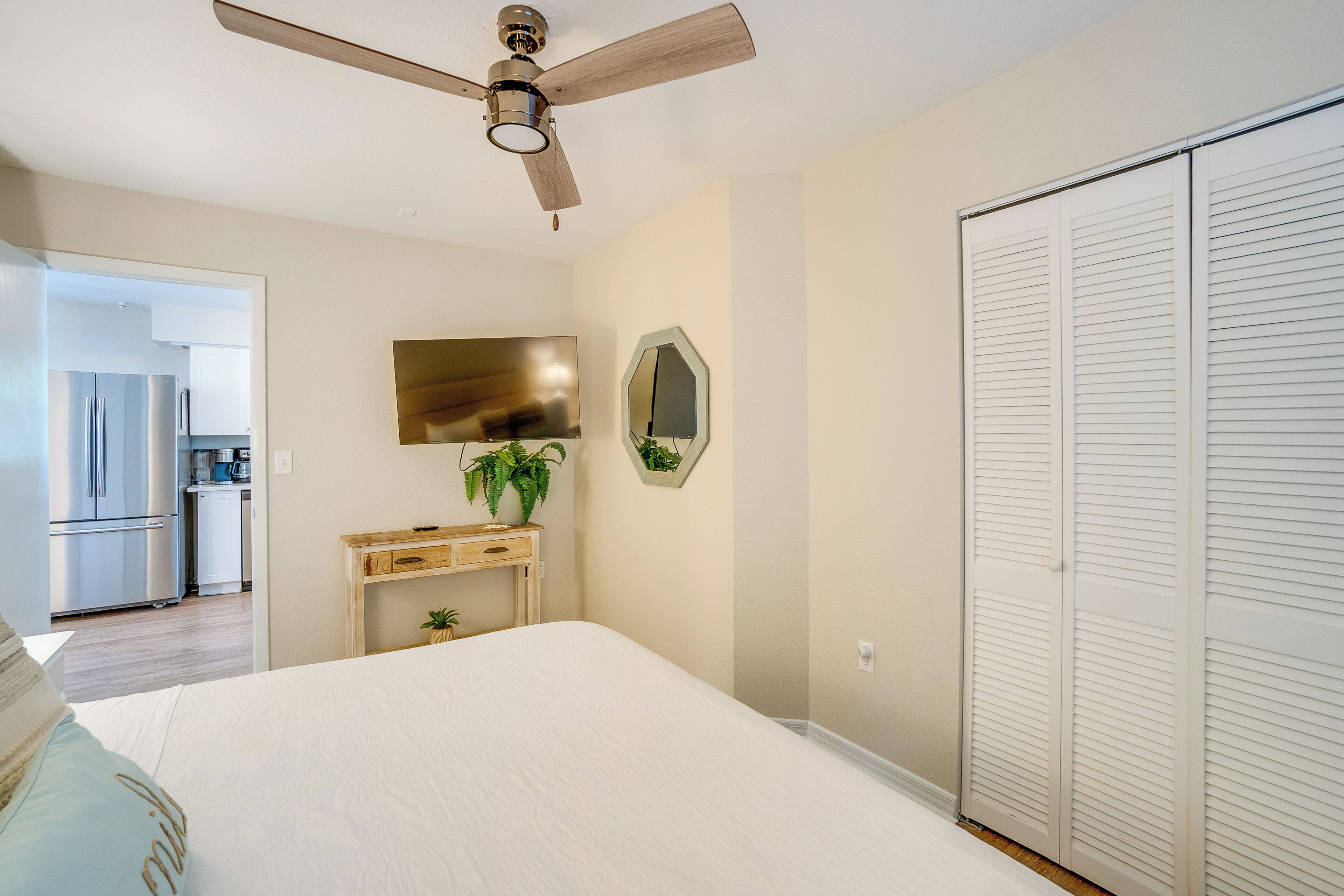Ein Schlafzimmer mit Bett, Deckenventilator, Fernseher, Spiegel und Kleiderschrank.