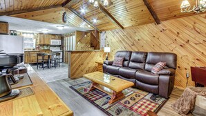 A cozy cabin interior with a wooden ceiling, a leather sofa, a dining table, and a kitchen area. - Lake Access & Hot Tub! Serene Rockbridge Cabin (Amanda)