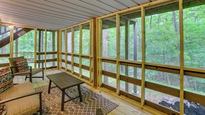 A covered outdoor seating area with wooden benches and a table, large windows, and a view of a forest. - Lake Access & Hot Tub! Serene Rockbridge Cabin (Amanda)