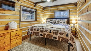 A log cabin bedroom with a bed, a dresser, a ceiling fan, and two windows. - Lake Access & Hot Tub! Serene Rockbridge Cabin (Amanda)